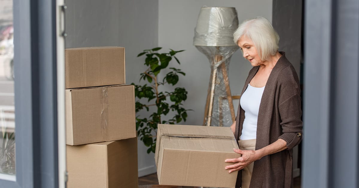 Over 50s lady holding a box in front of a stack of boxes