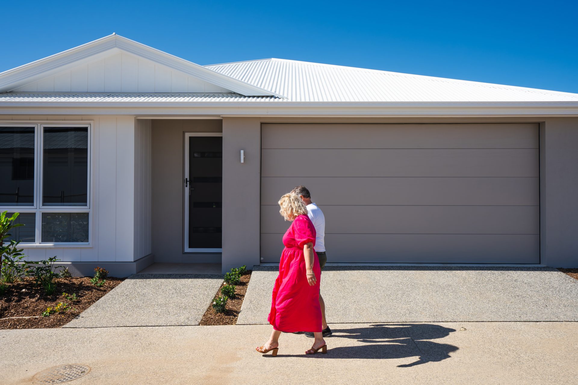 Living Gems Moreton Bay residents Will and Tina Fedder walking together outside their modern villa on a sunny day.