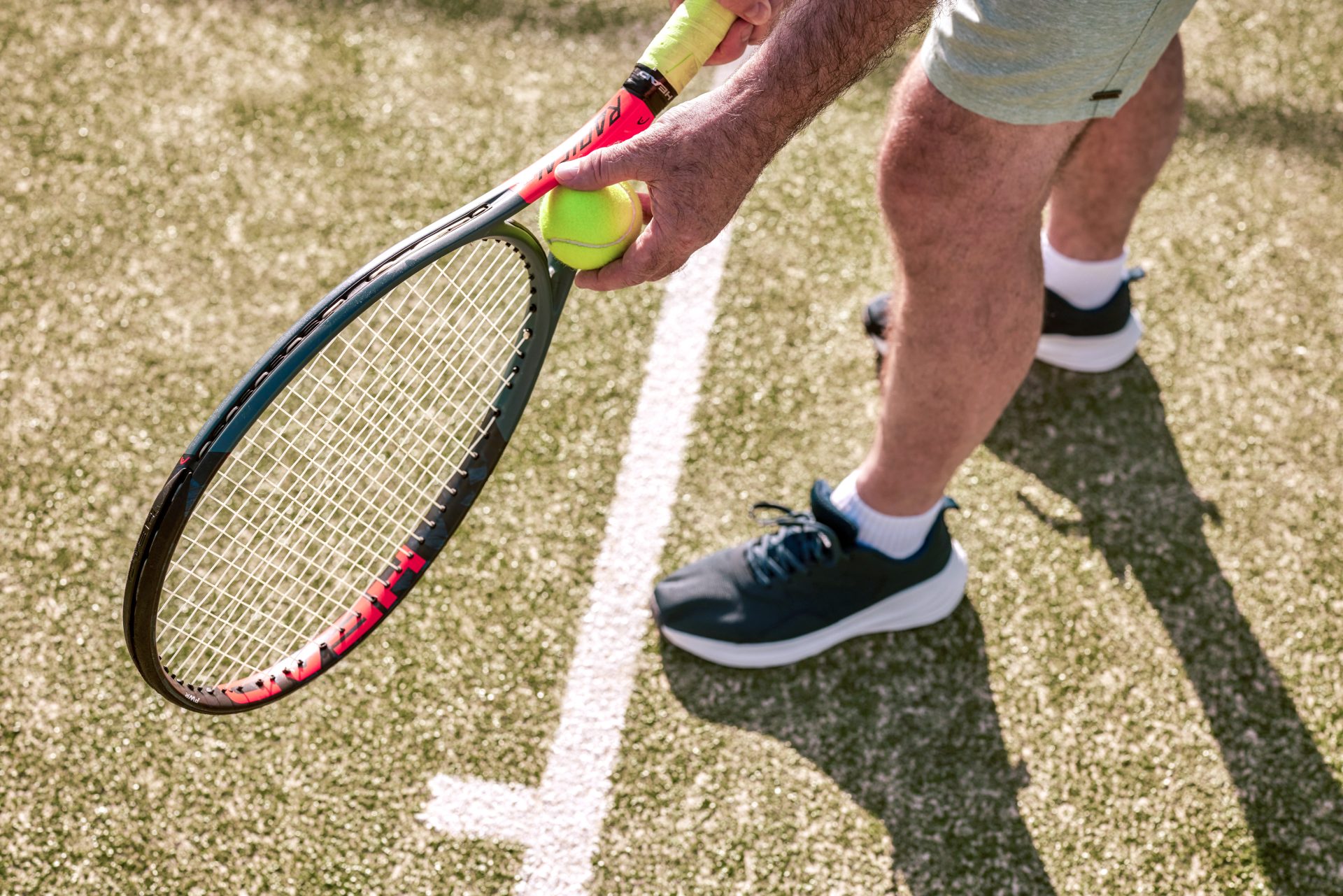 Close-up of a tennis player holding a racquet and tennis ball on a grass court, ready to serve.